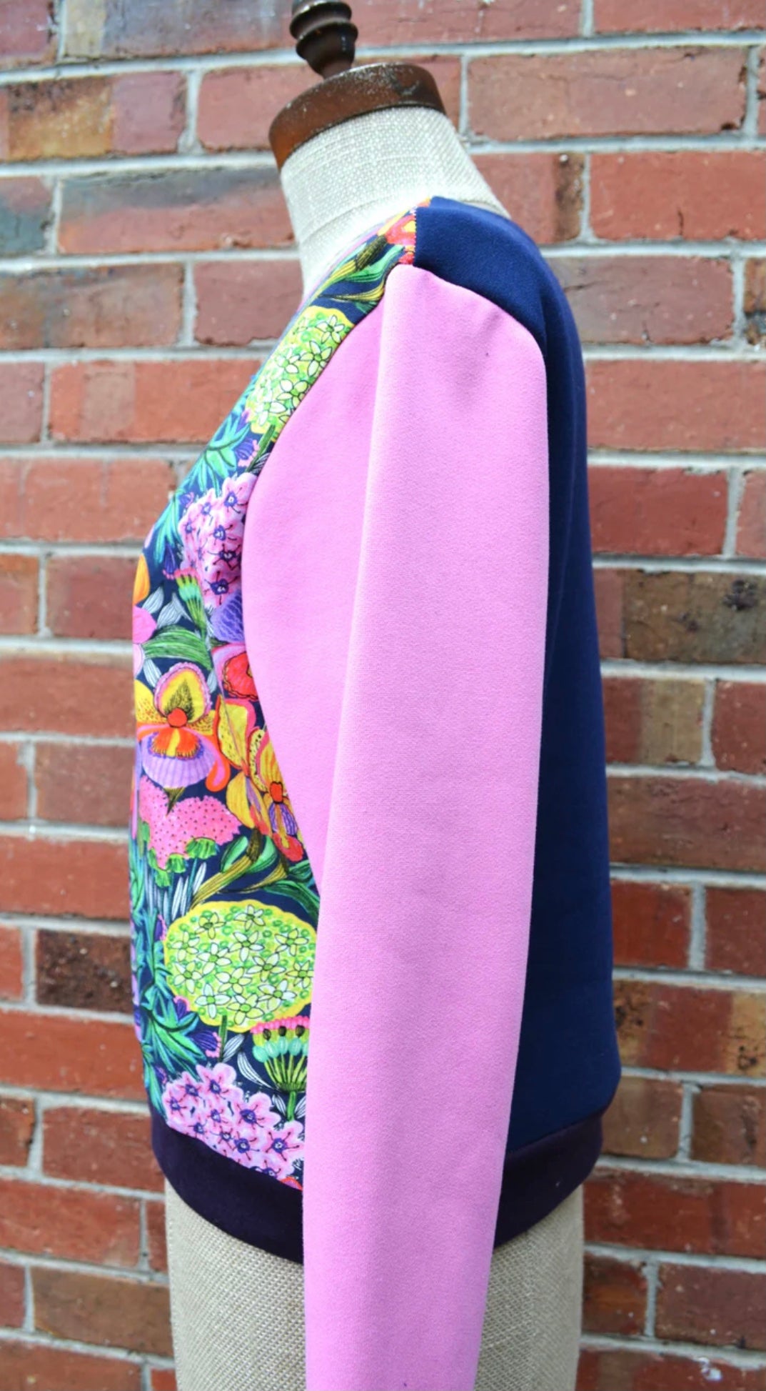 Colorful floral-patterned garment on a mannequin against a brick wall.