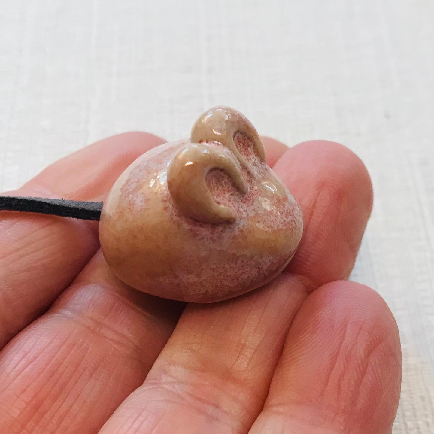 Hand holding a small brown ceramic duck-shaped object against a white background