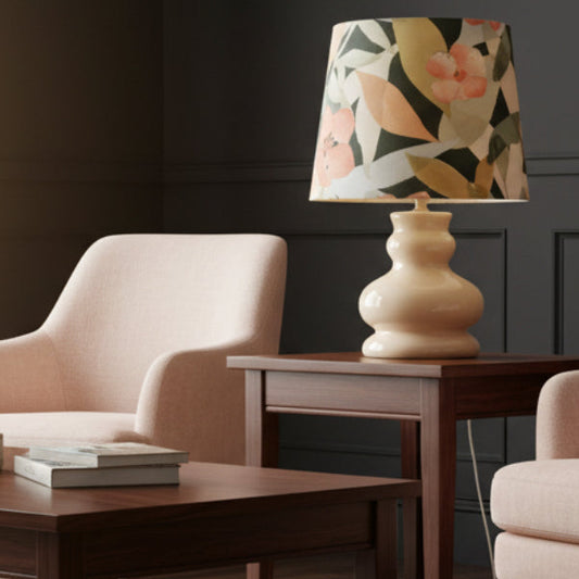 Floral-patterned lamp on a wooden table with a chair and books in a room.