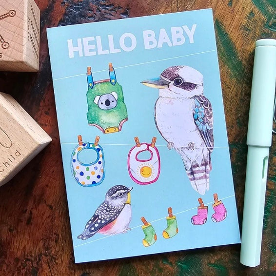 greeting card titled 'Hello Baby' with illustrations of birds and baby items on a wooden surface.
