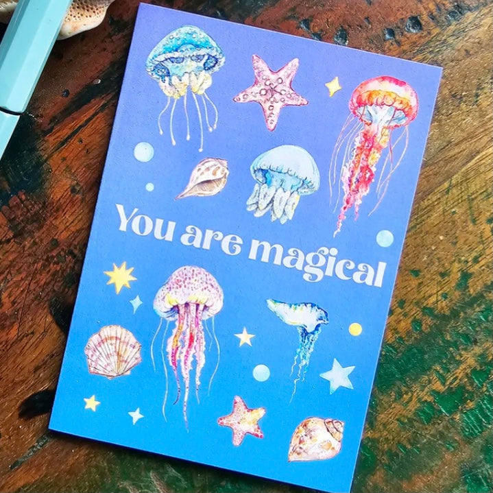 greeting card with sea creature illustrations and 'You are magical' text on a wooden surface