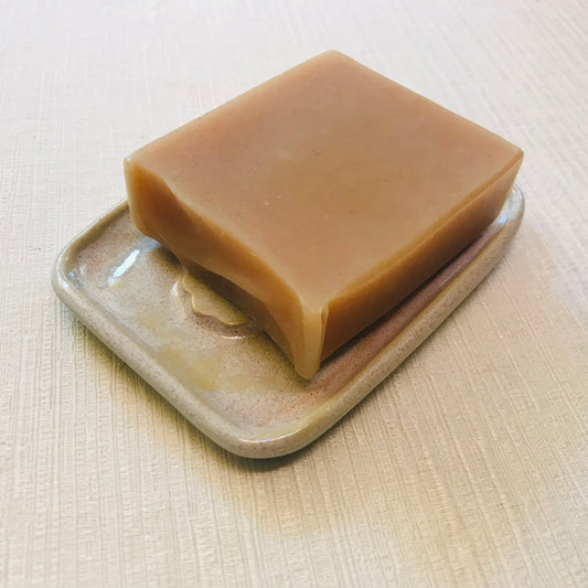 Bar of soap on a ceramic soap dish against a neutral background