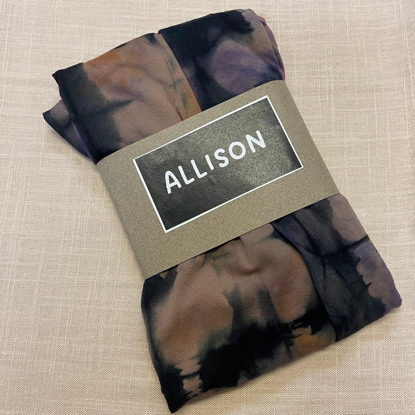 Folded tie dyed womens tights with a label reading 'ALLISON' on a beige background