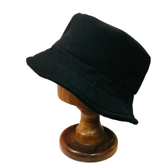 Black bucket hat on a wooden mannequin head against a beige background
