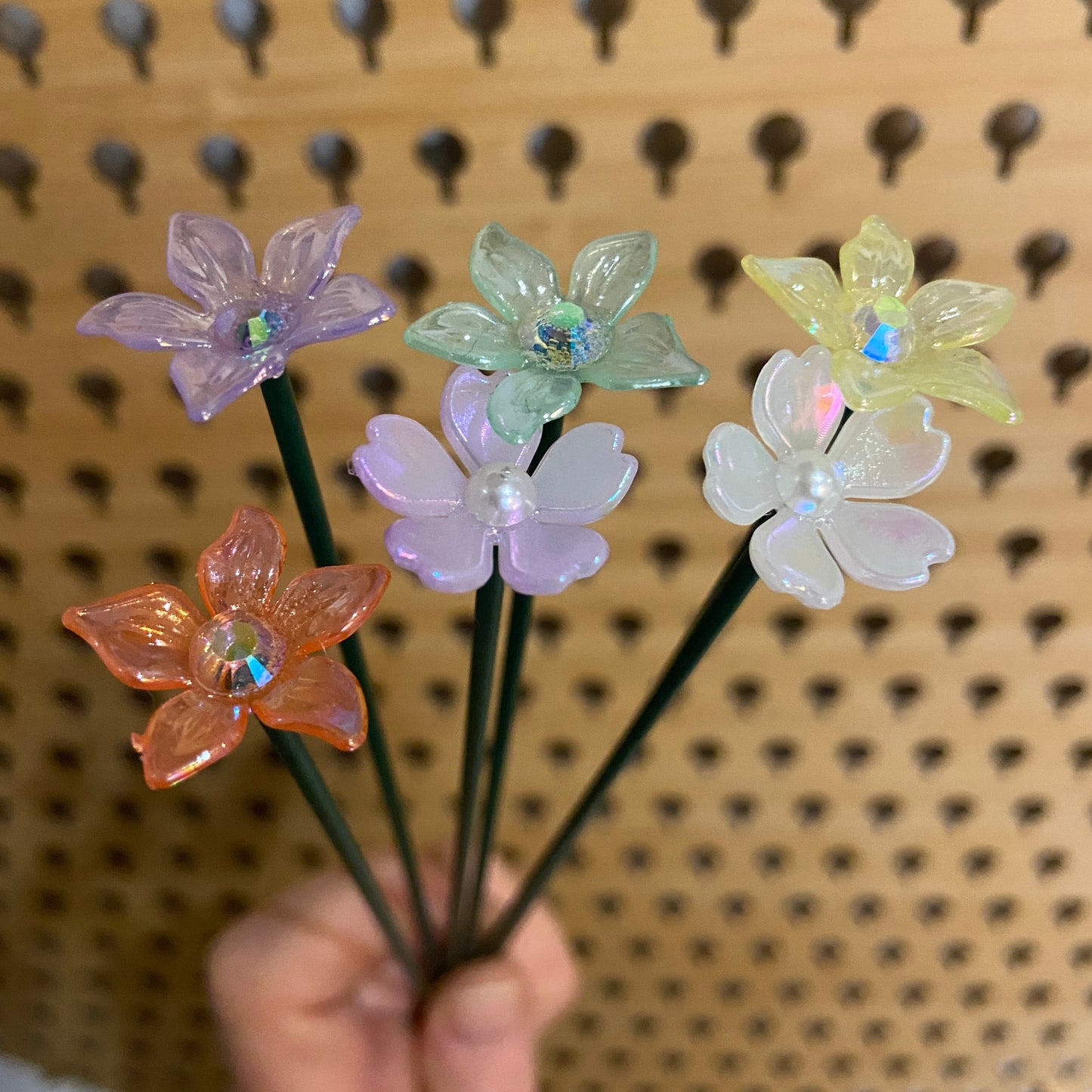 Hand holding colorful artificial flowers against a textured beige background