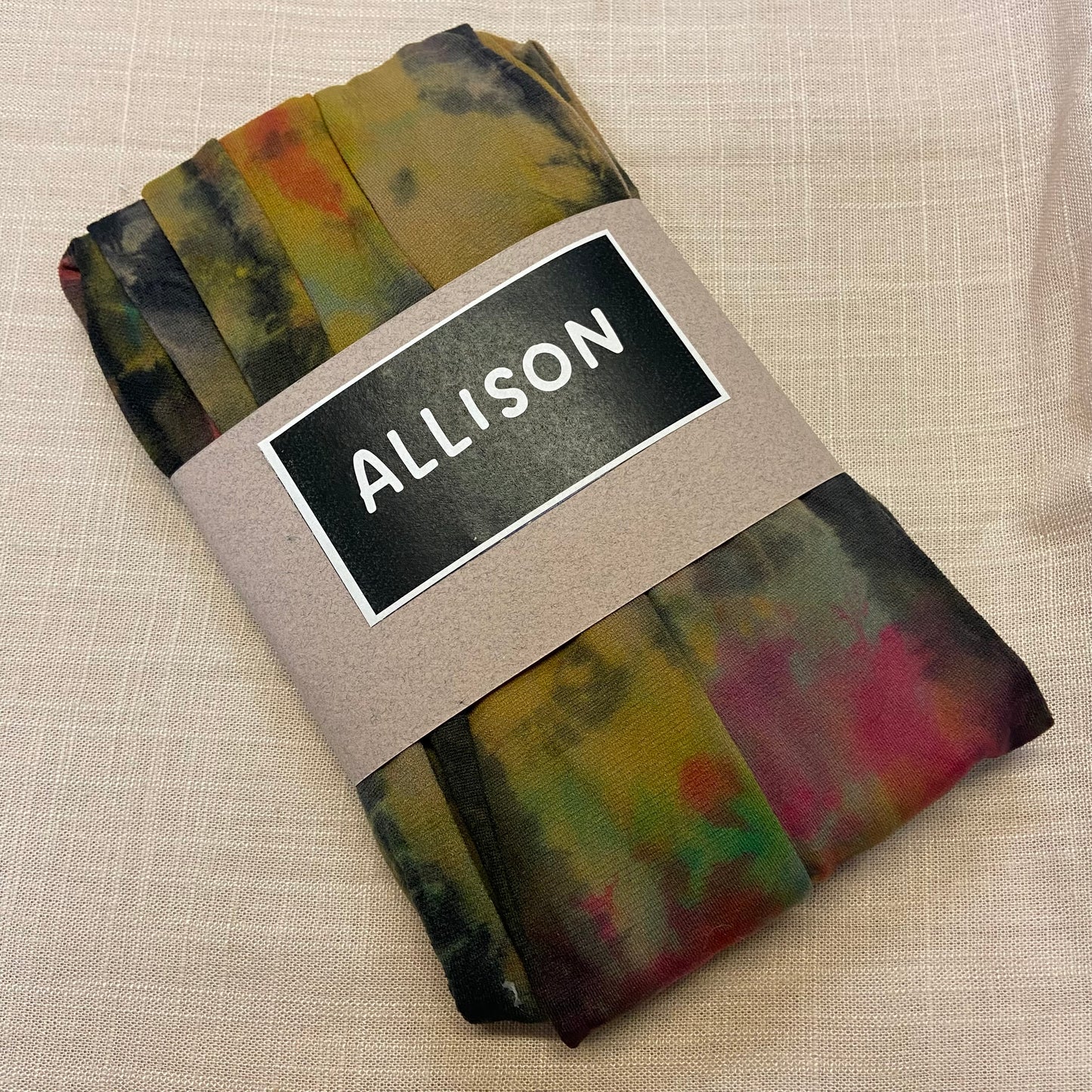 Folded tie dyed womens tights with a label reading 'ALLISON' on a beige background