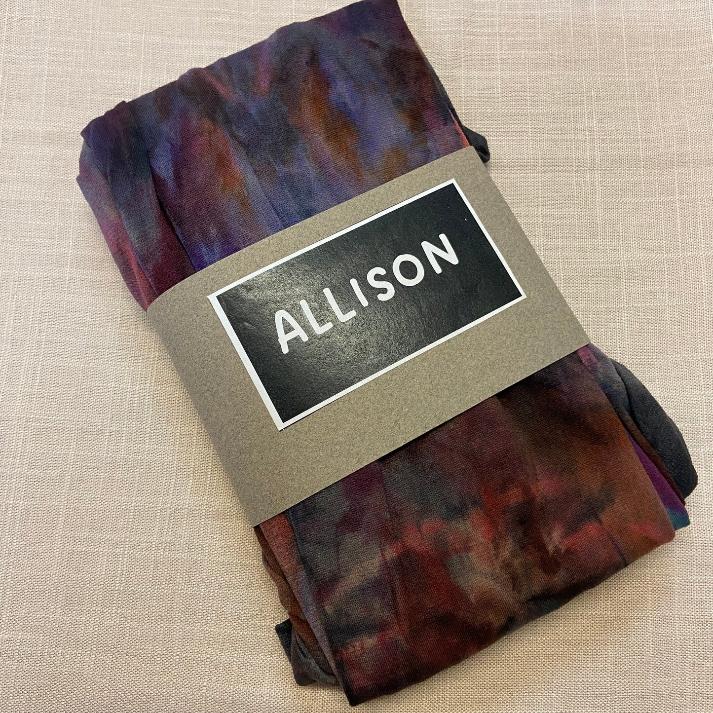 Folded tie dyed womens tights with a label reading 'ALLISON' on a beige background