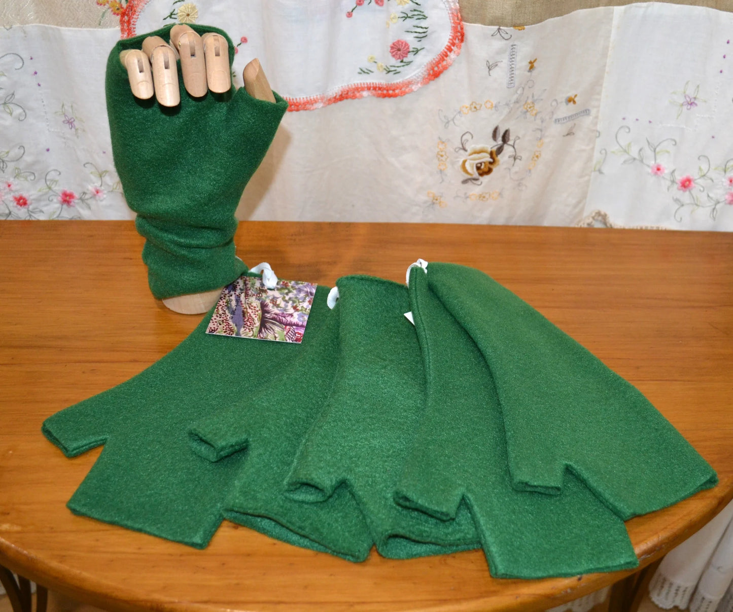 Green fingerless gloves on a wooden table with a floral-patterned fabric background