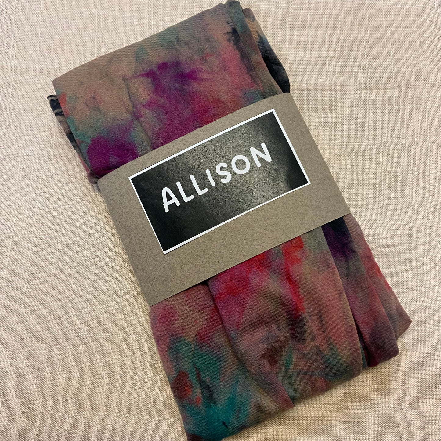 Folded tie dyed womens tights with a label reading 'ALLISON' on a beige background