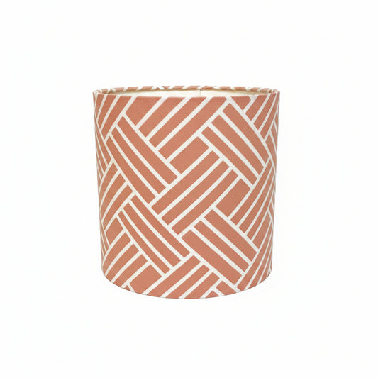 A cylindrical lampshade featuring a terracotta orange and white geometric herringbone pattern, set against a plain white background.