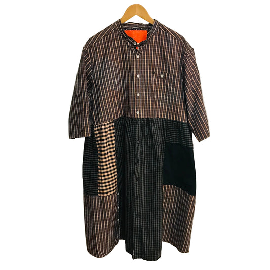 Plaid dress with patchwork design on a hanger against a white wall