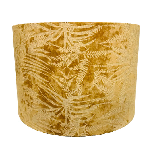 A cylindrical drum lampshade made of textured mustard yellow velvet with an embossed or woven fern leaf pattern