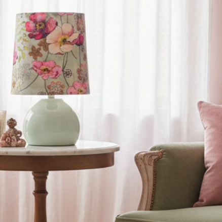 Small lamp with a floral-patterned shade on a side table in a living room with pink and green tones