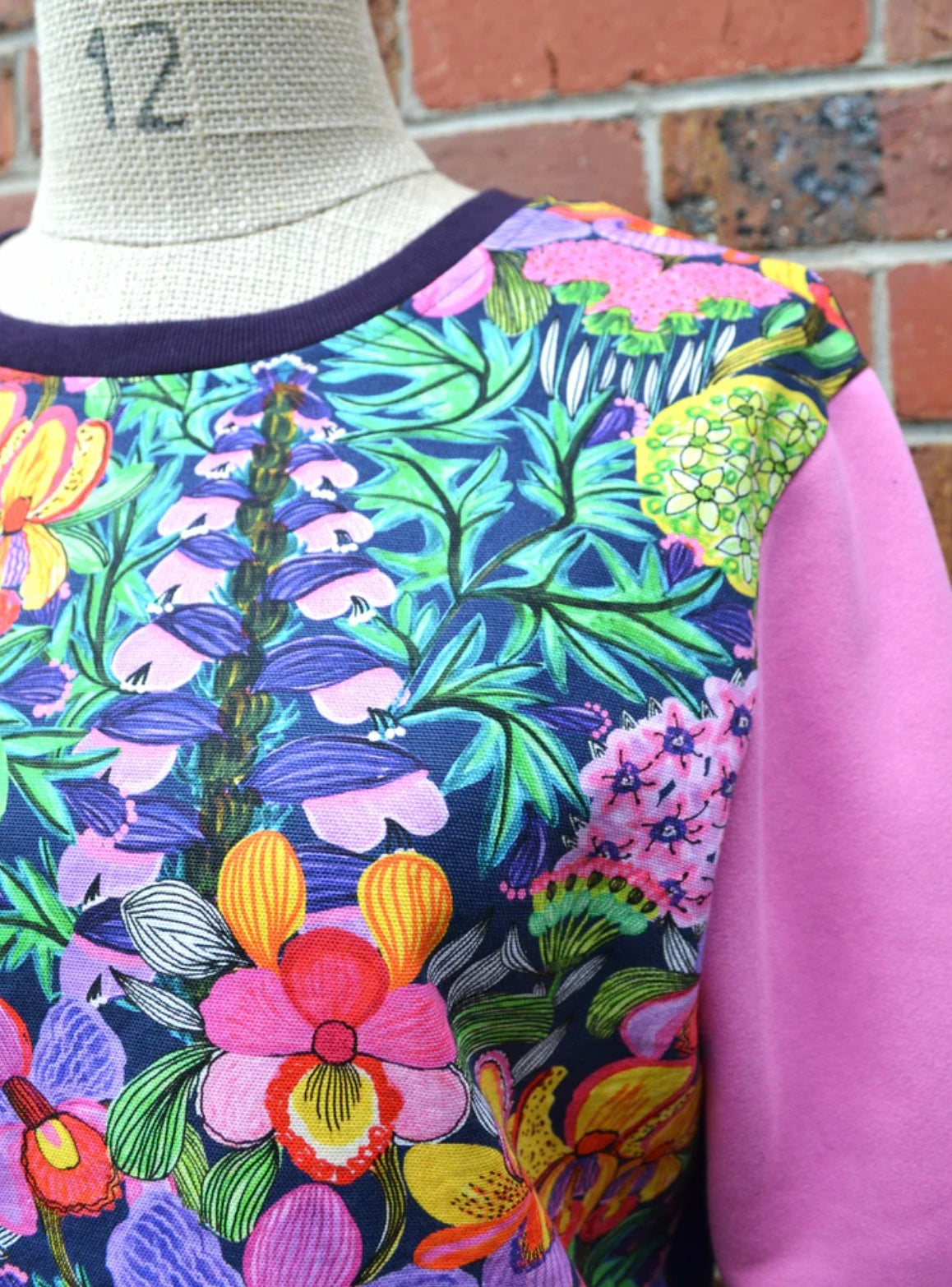 Colorful floral-patterned garment on a mannequin against a brick wall.