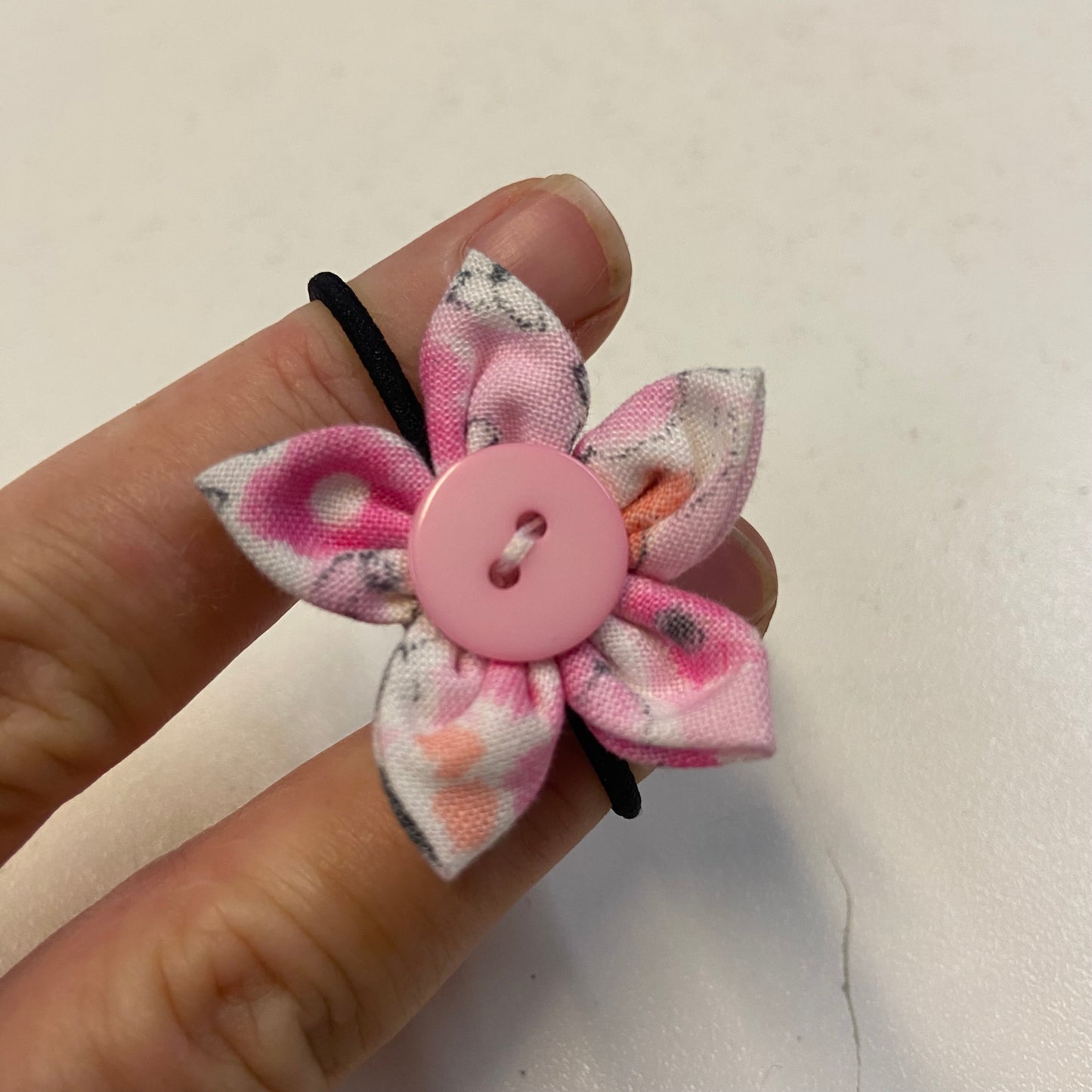 Hand holding a pink flower-shaped hairtie with a button center on a light background