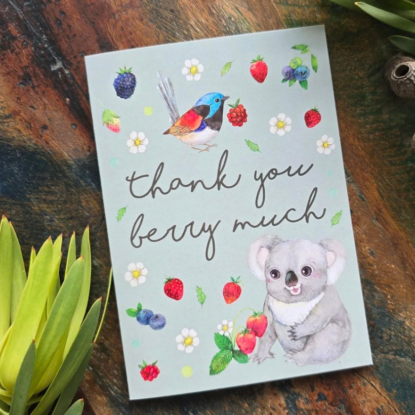 Greeting card with a koala, bird, and berries on a wooden surface