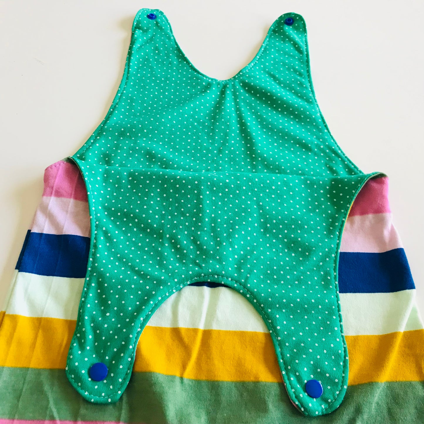 Green polka dot lining on a baby romper with colorful striped pattern on a light background