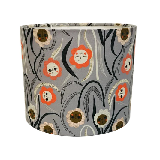 A cylindrical lampshade with a gray background and a whimsical floral pattern featuring orange, white, black, and brown stylized flowers and leaves.