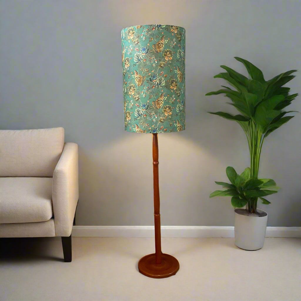 Floor lamp with a decorative green and gold shade in a room with a sofa and plant.