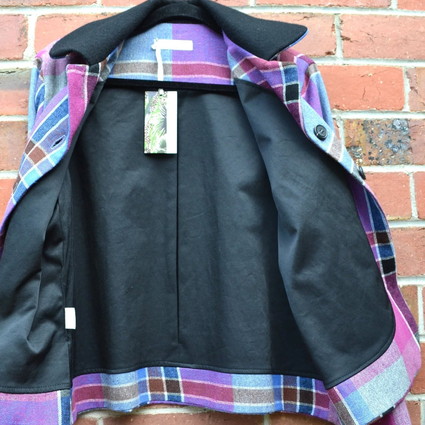 Plaid cropped jacket with black lining and tag on a brick wall background