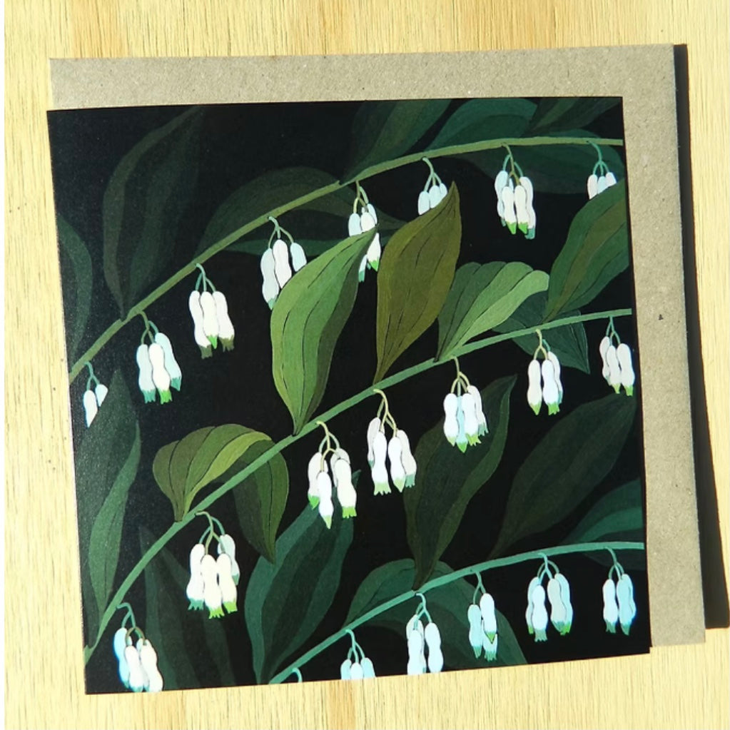 greeting Card with white flowers and green leaves on a black background, placed on a wooden surface.