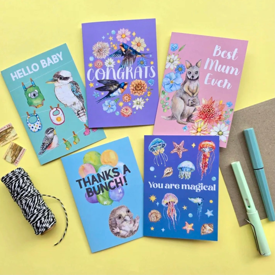 Five colorful greeting cards on a yellow background with stationery items.