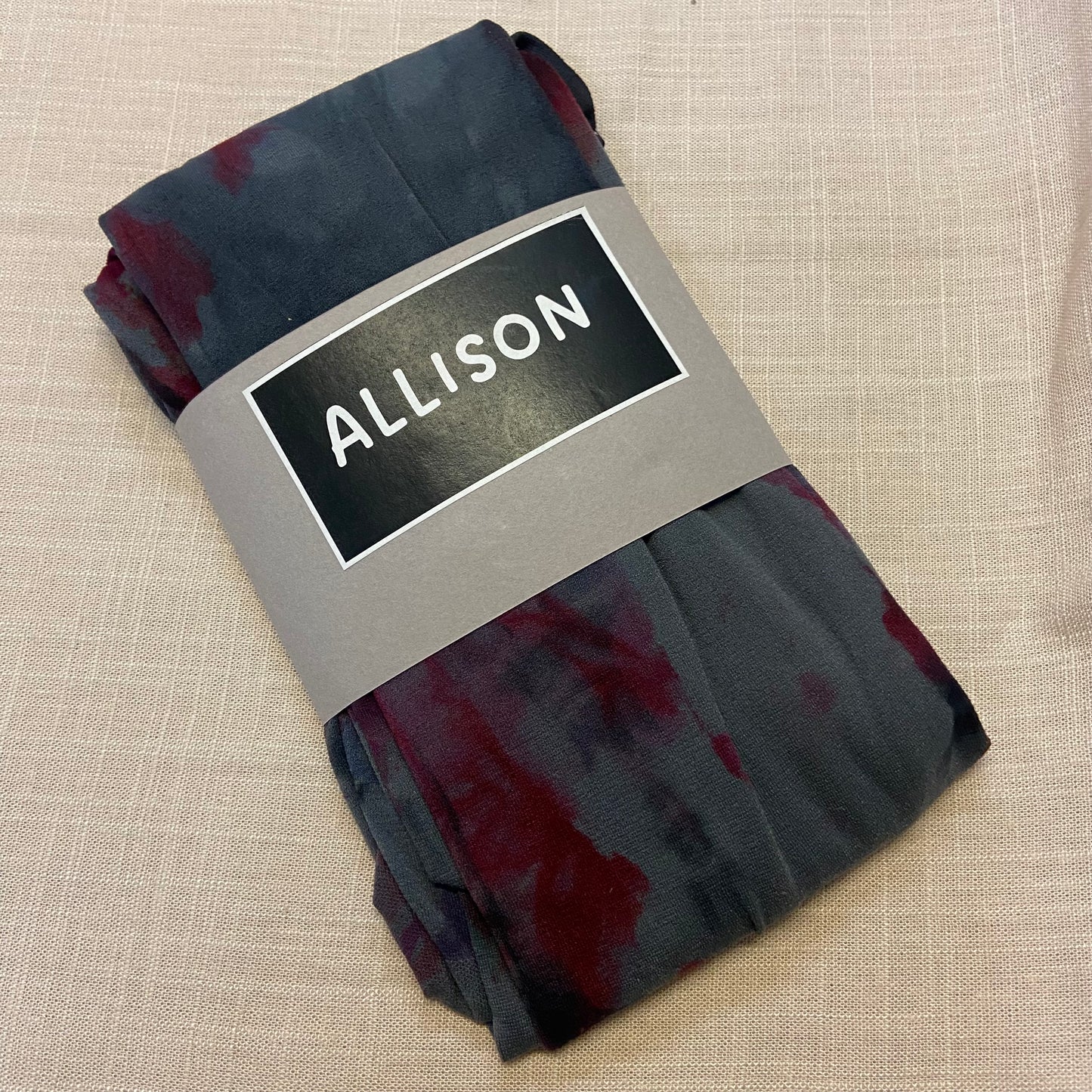 Folded hand dyed tights with 'ALLISON' label on a beige textured background