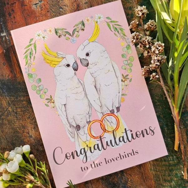 Card with illustration of two parrots and 'Congratulations to the lovebirds' text on a pink background.
