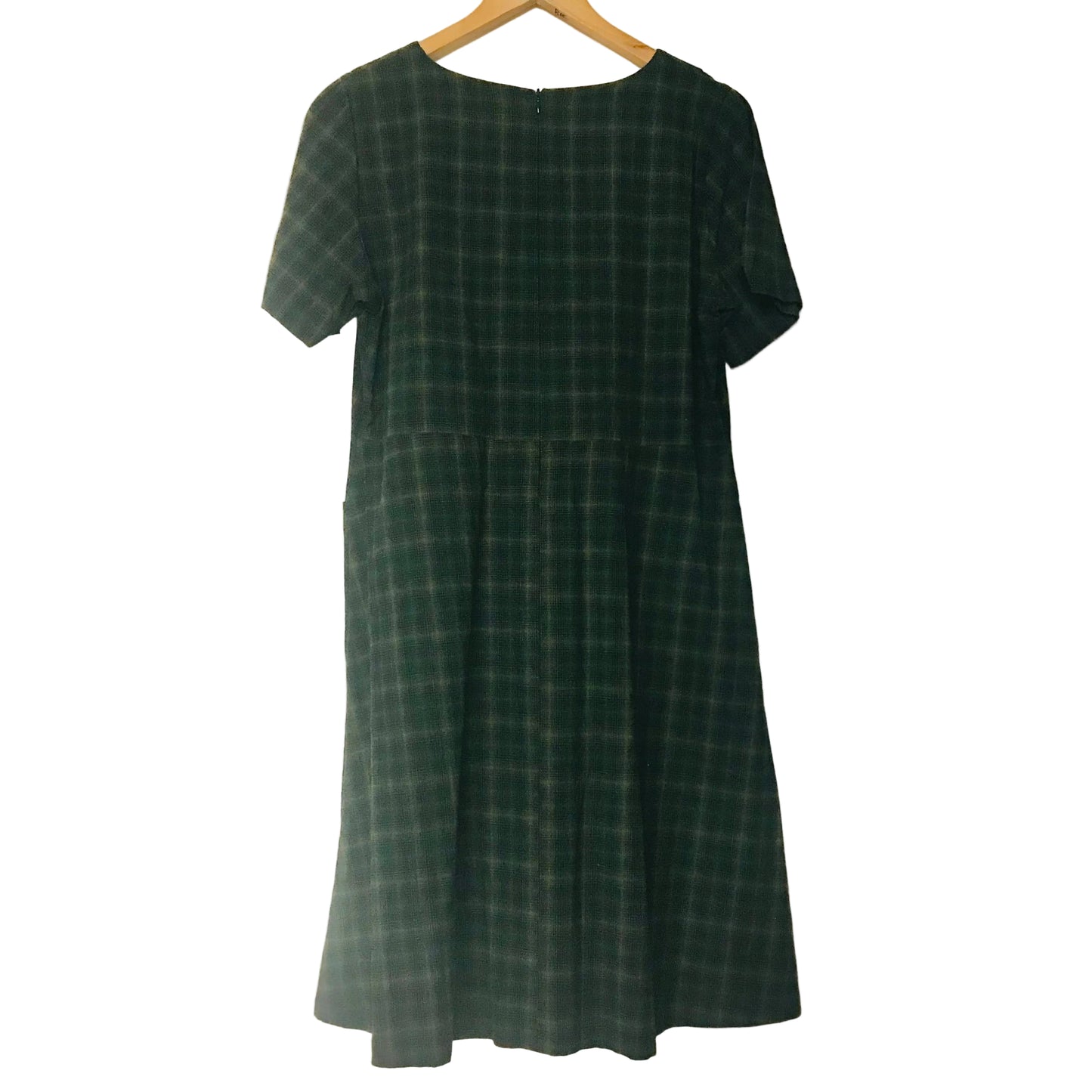 A dark green plaid short-sleeve dress hanging on a wooden hanger against a plain off-white wall.