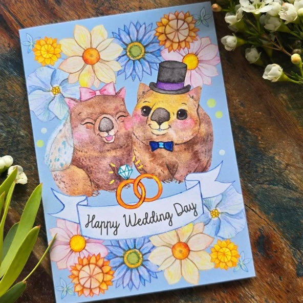 Wedding card with cartoon otters and floral decorations on a wooden surface.