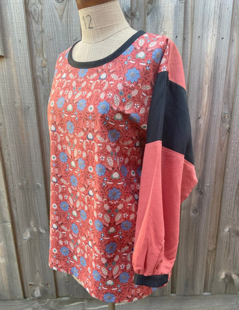 Floral-patterned tunic top with pink and black sleeves on a mannequin against a wooden fence background