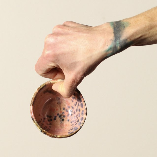Hand holding a small wooden bowl with a speckled pattern against a beige background