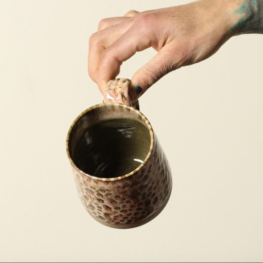 Hand holding a textured ceramic mug against a beige background