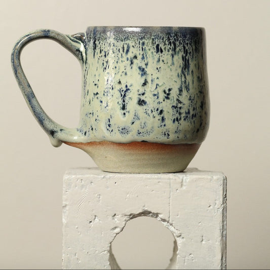 Speckled ceramic mug on a white pedestal against a beige background