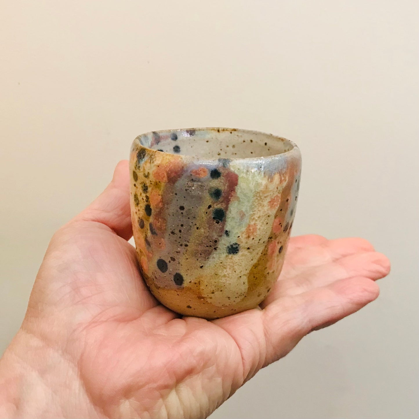 Hand holding a small ceramic cup with speckled glaze against a plain background