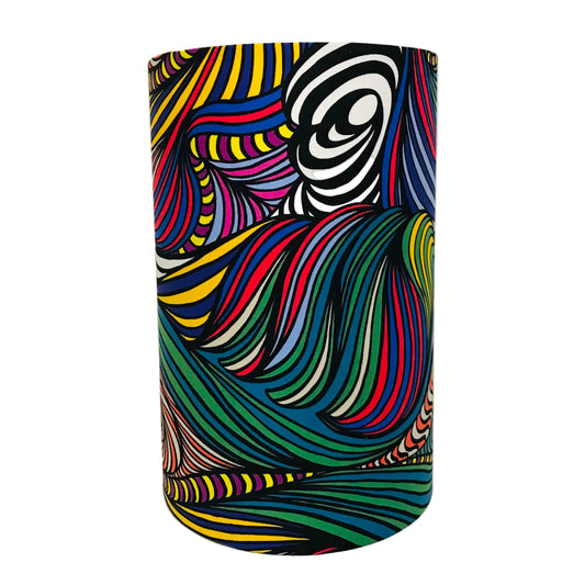 A cylindrical lampshade featuring a vibrant, psychedelic abstract pattern of swirling, wavy stripes in multiple colors including yellow, blue, green, red, pink, purple, black, and white, set against a plain white background.