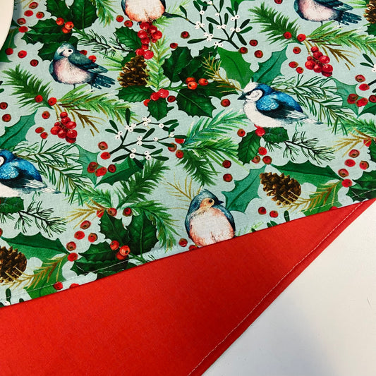 Christmas-themed placemats with birds, holly, and berries with red on reverse