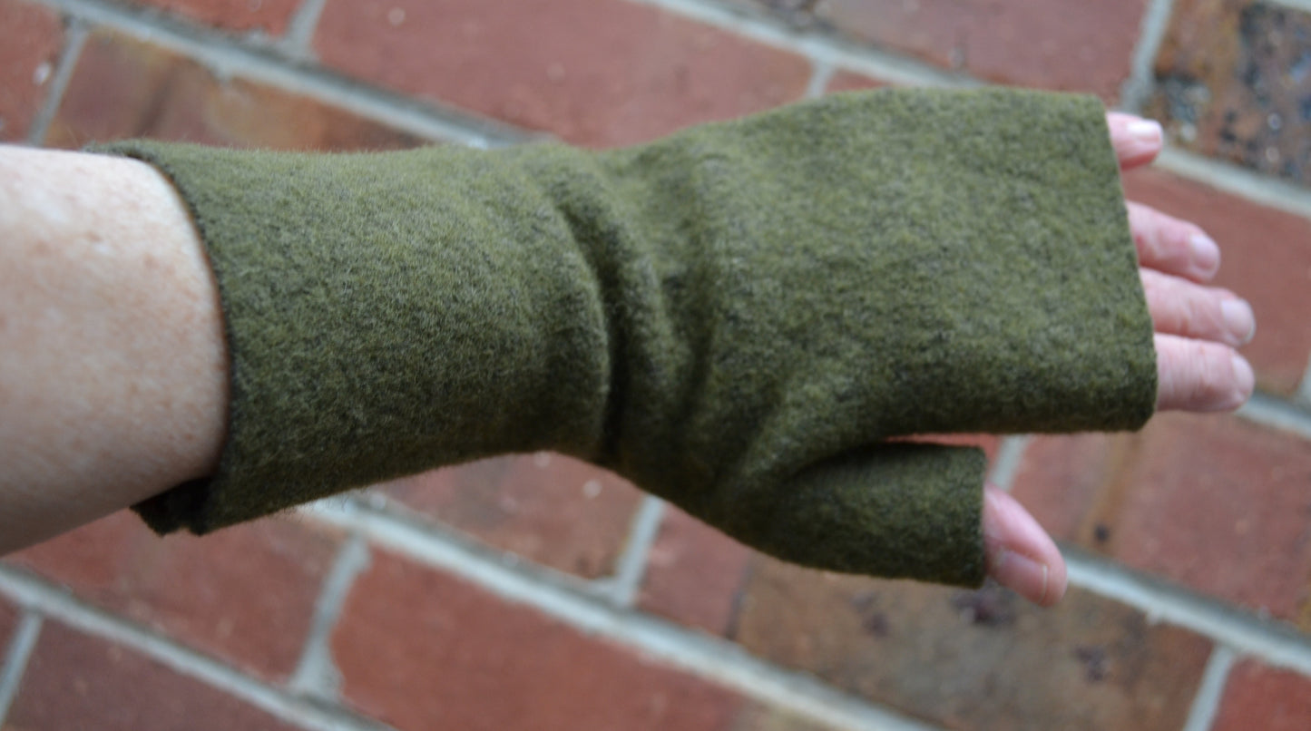 Green fingerless gloves worn on a person's hand against a brick wall background