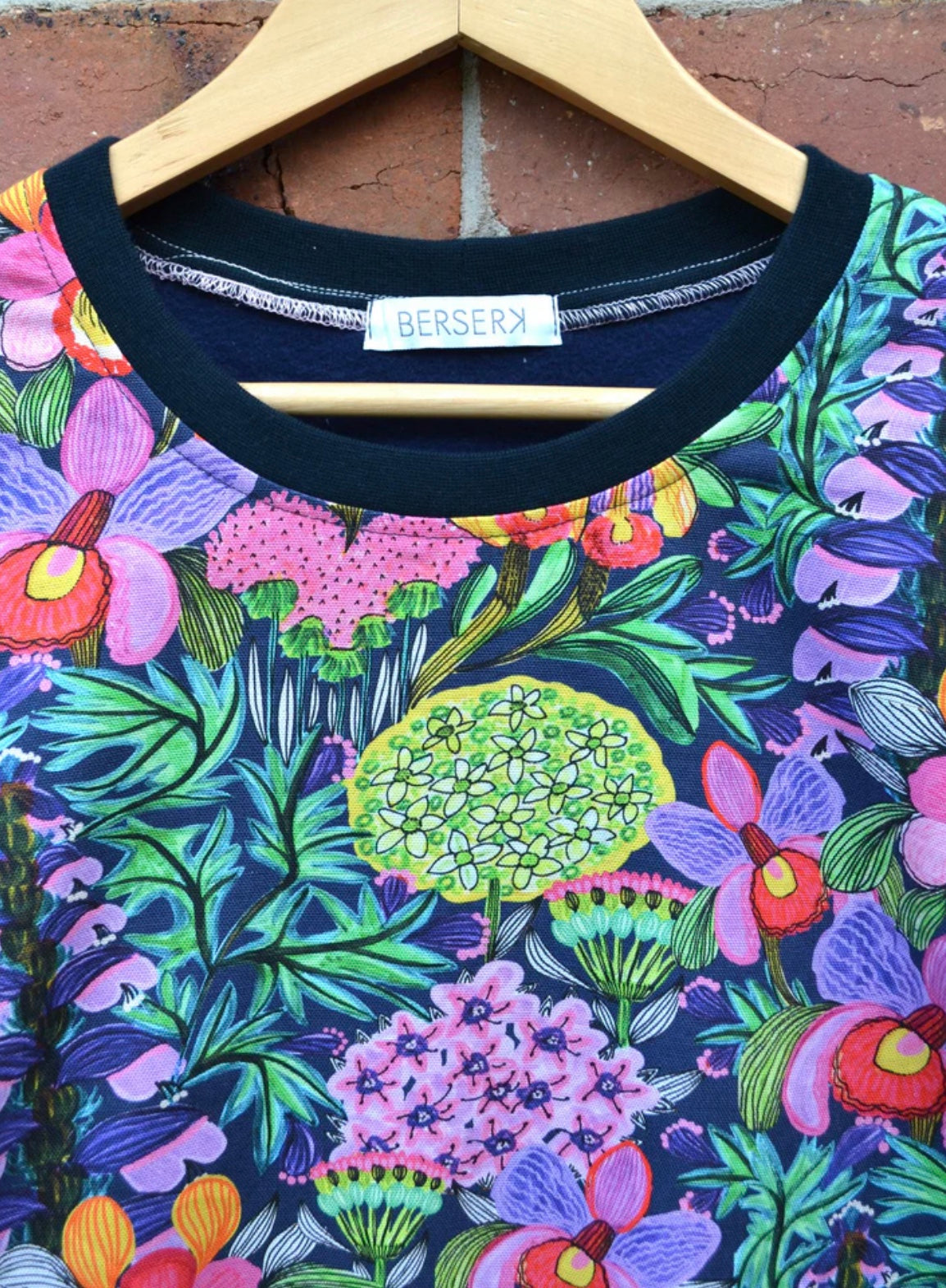 Colorful floral-patterned sweater on a hanger with 'Berserk' branding.