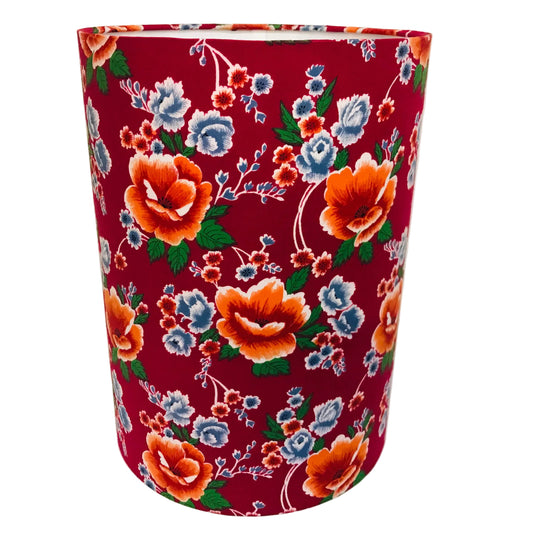 A cylindrical lampshade featuring a vibrant red background with a detailed floral print of orange, blue, and white flowers with green leaves.