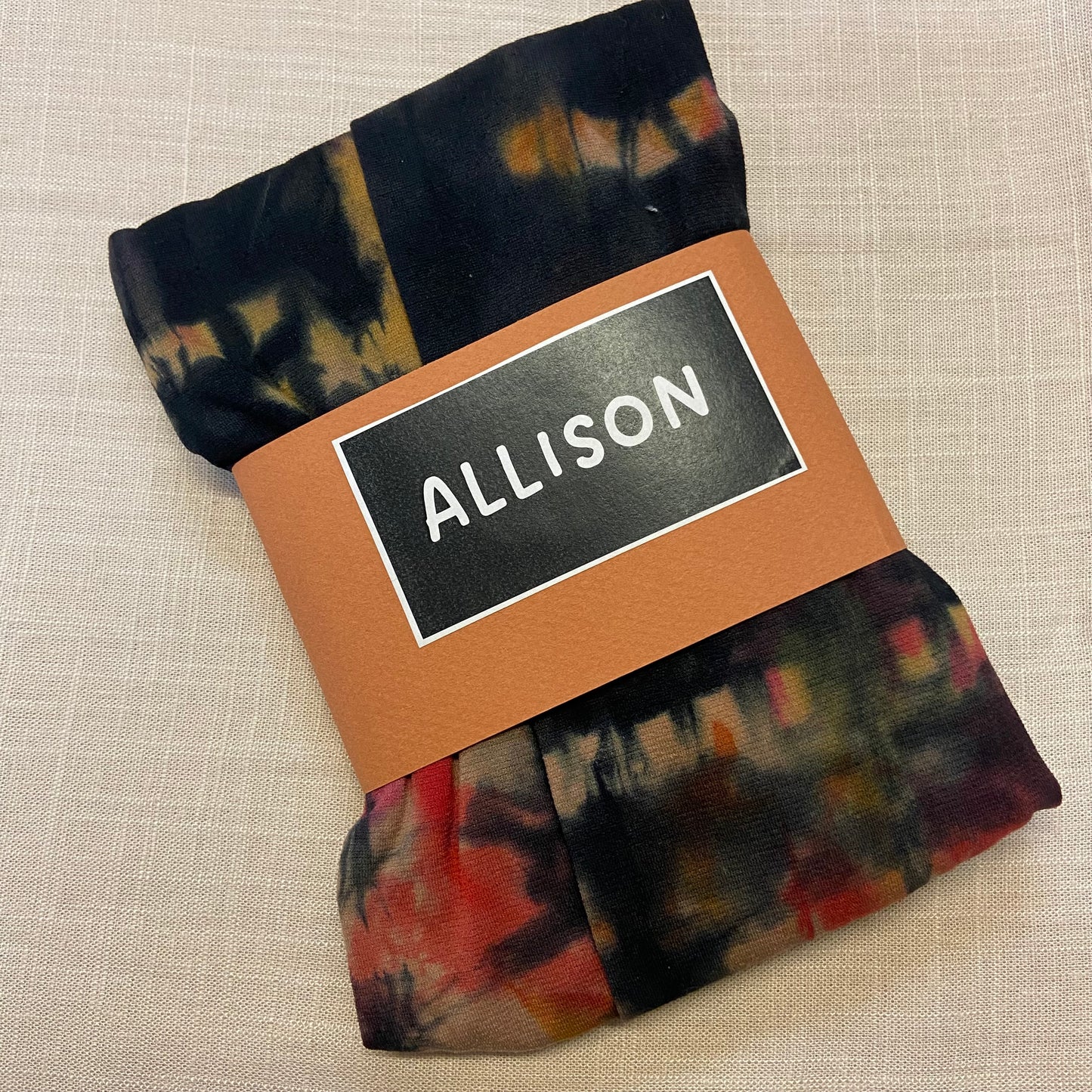 Folded tie dyed womens tights with a label reading 'ALLISON' on a beige background