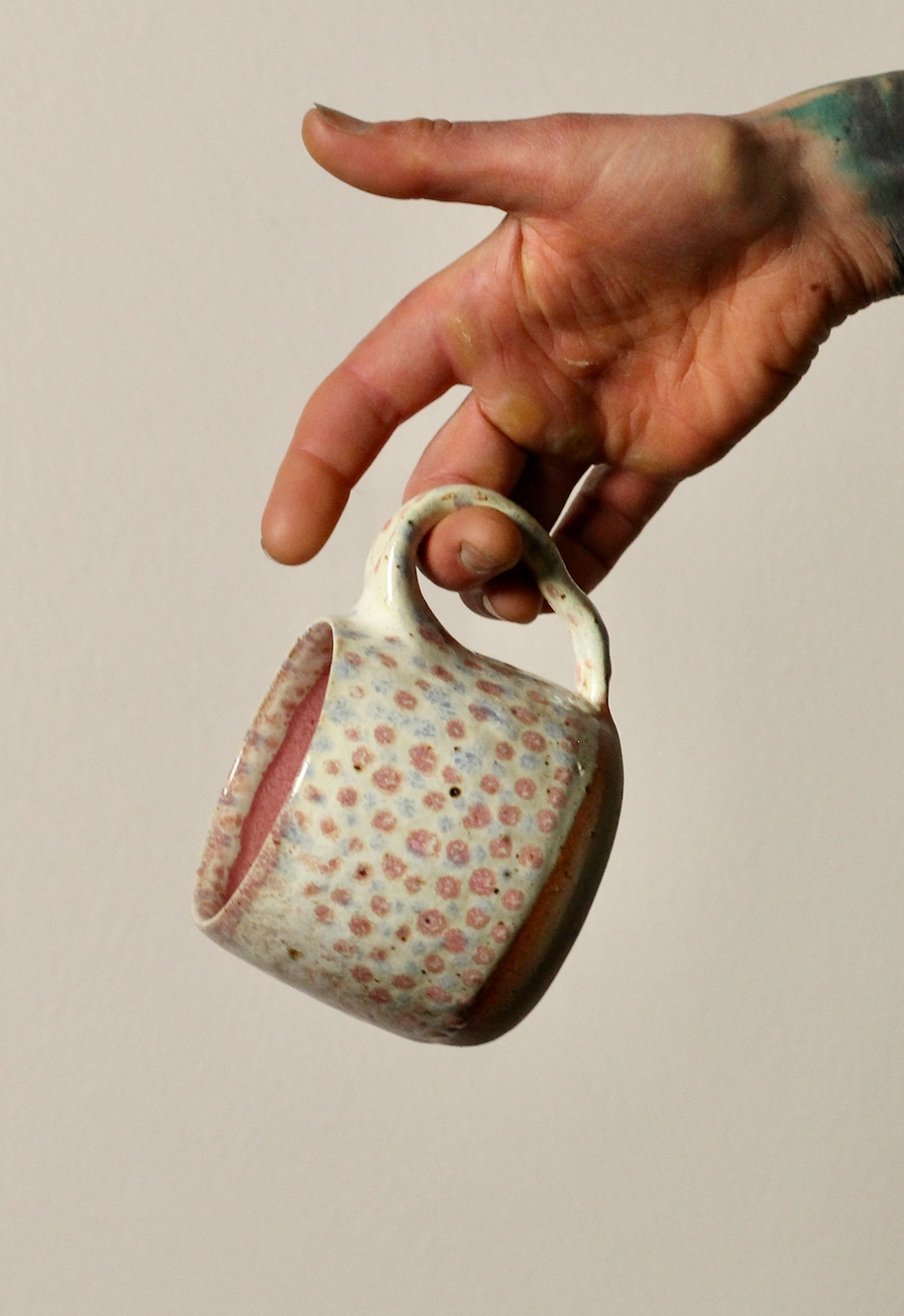 Hand holding a ceramic mug with spotty pattern against a neutral background