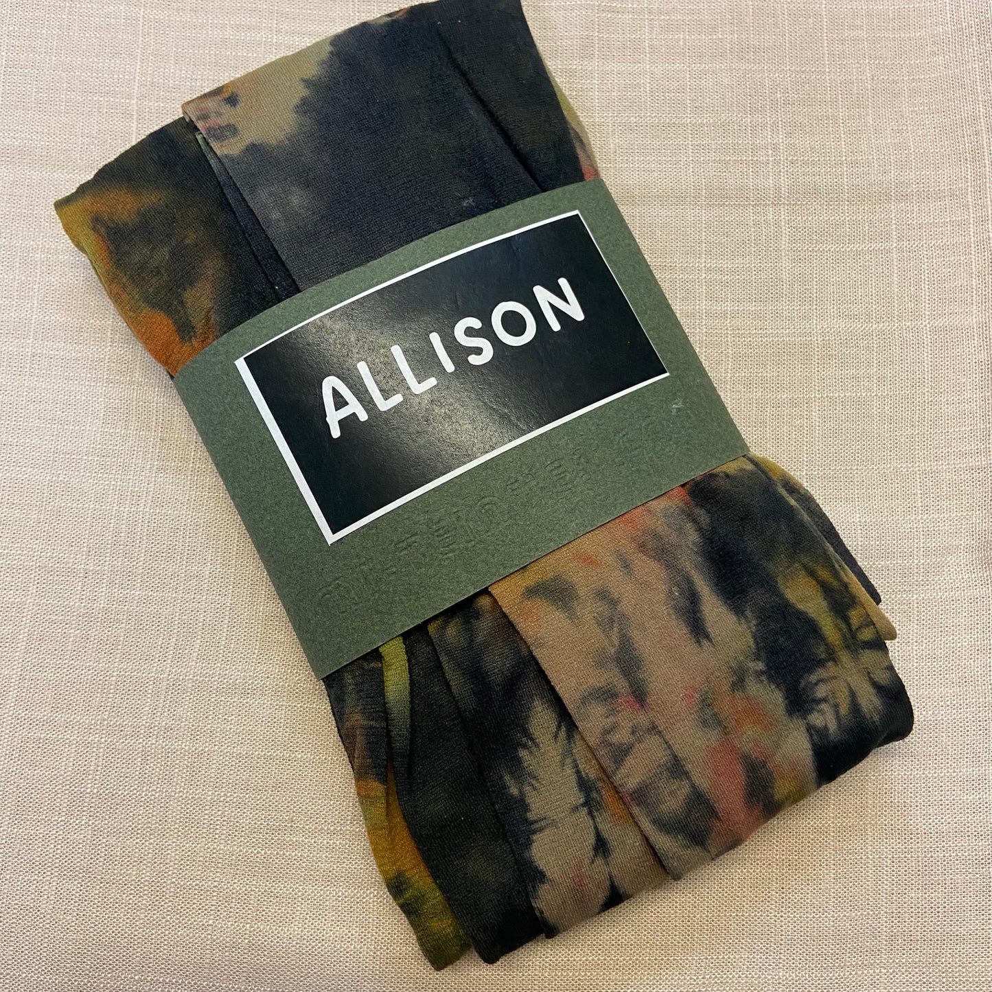 Folded tie dyed womens tights with a label reading 'ALLISON' on a beige background
