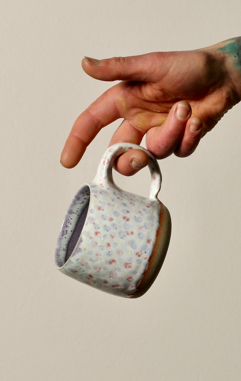 Hand holding a ceramic mug with floral pattern against a plain background