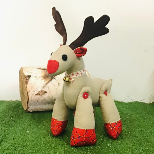 Toy reindeer with red shoes and antlers on a grassy surface with a white background