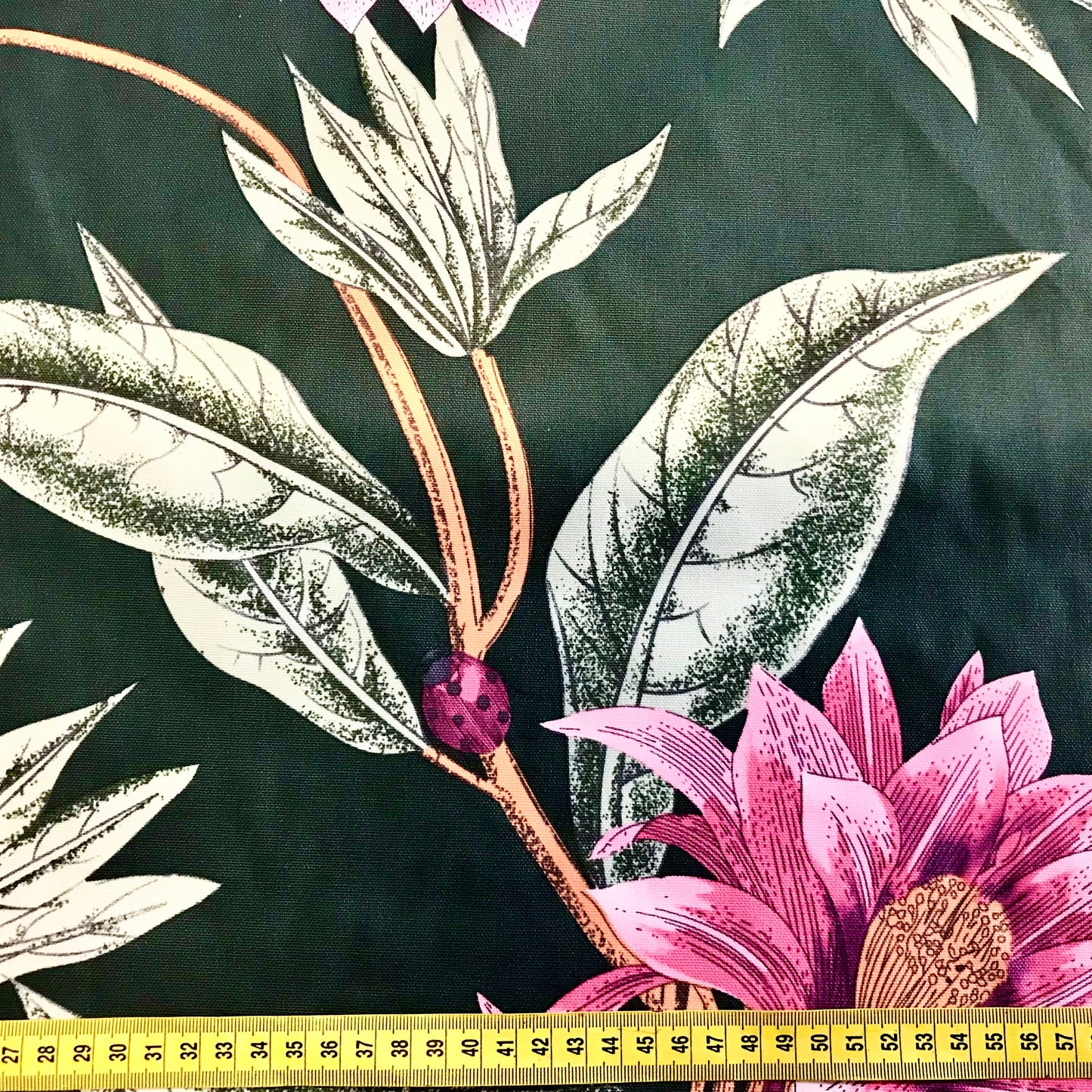 Floral and leaf pattern with a pink flower and purple bead on a dark background, measured with a ruler.