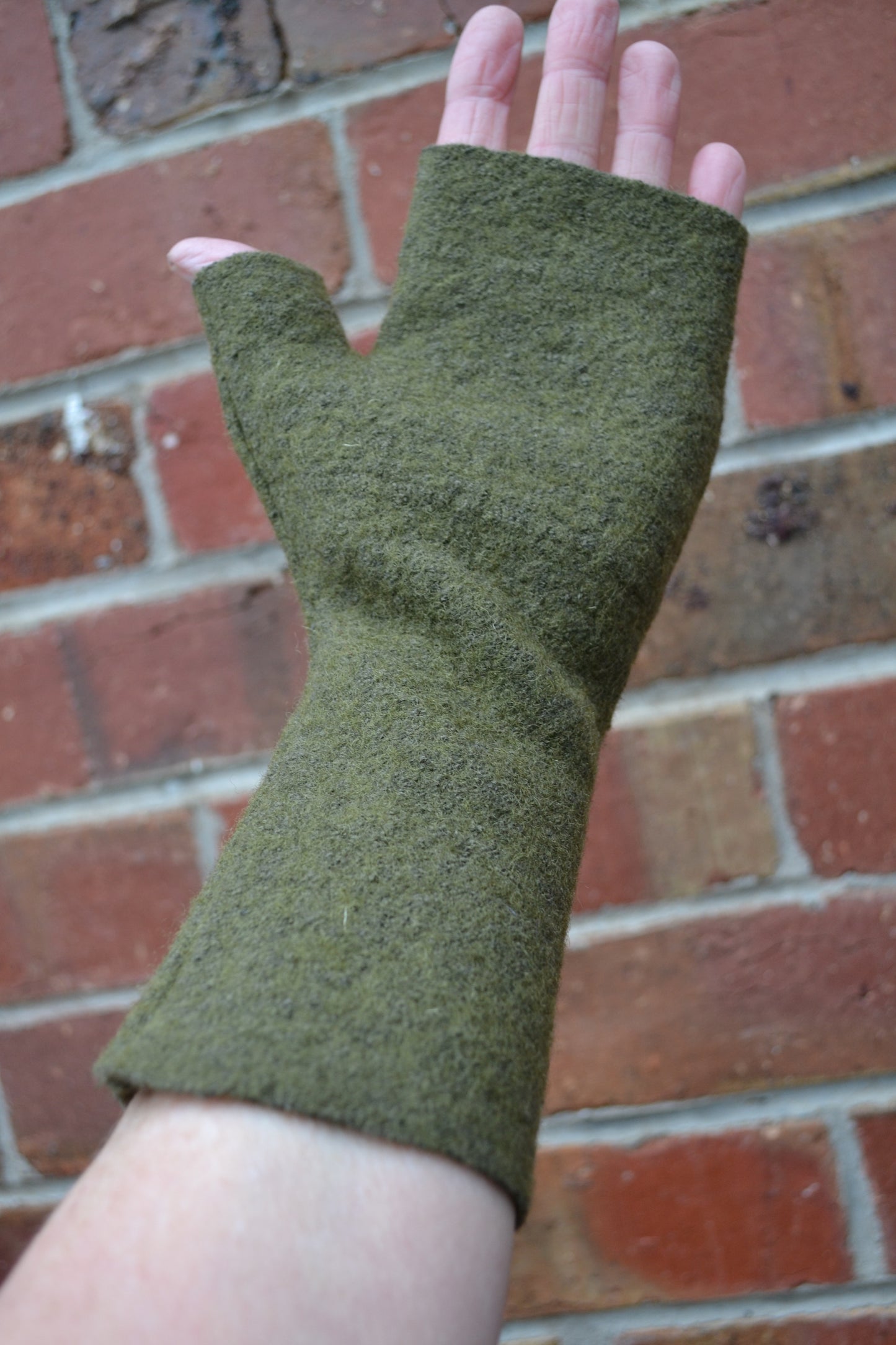 Green fingerless gloves worn on a hand with a brick background