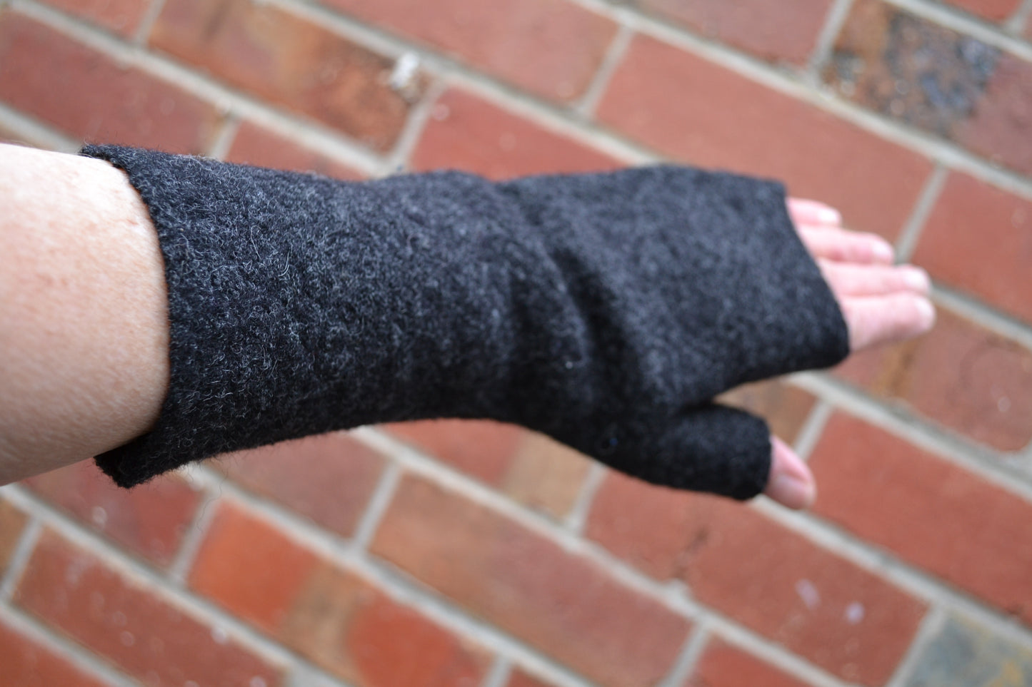 Black fingerless gloves worn on a wrist against a brick wall background