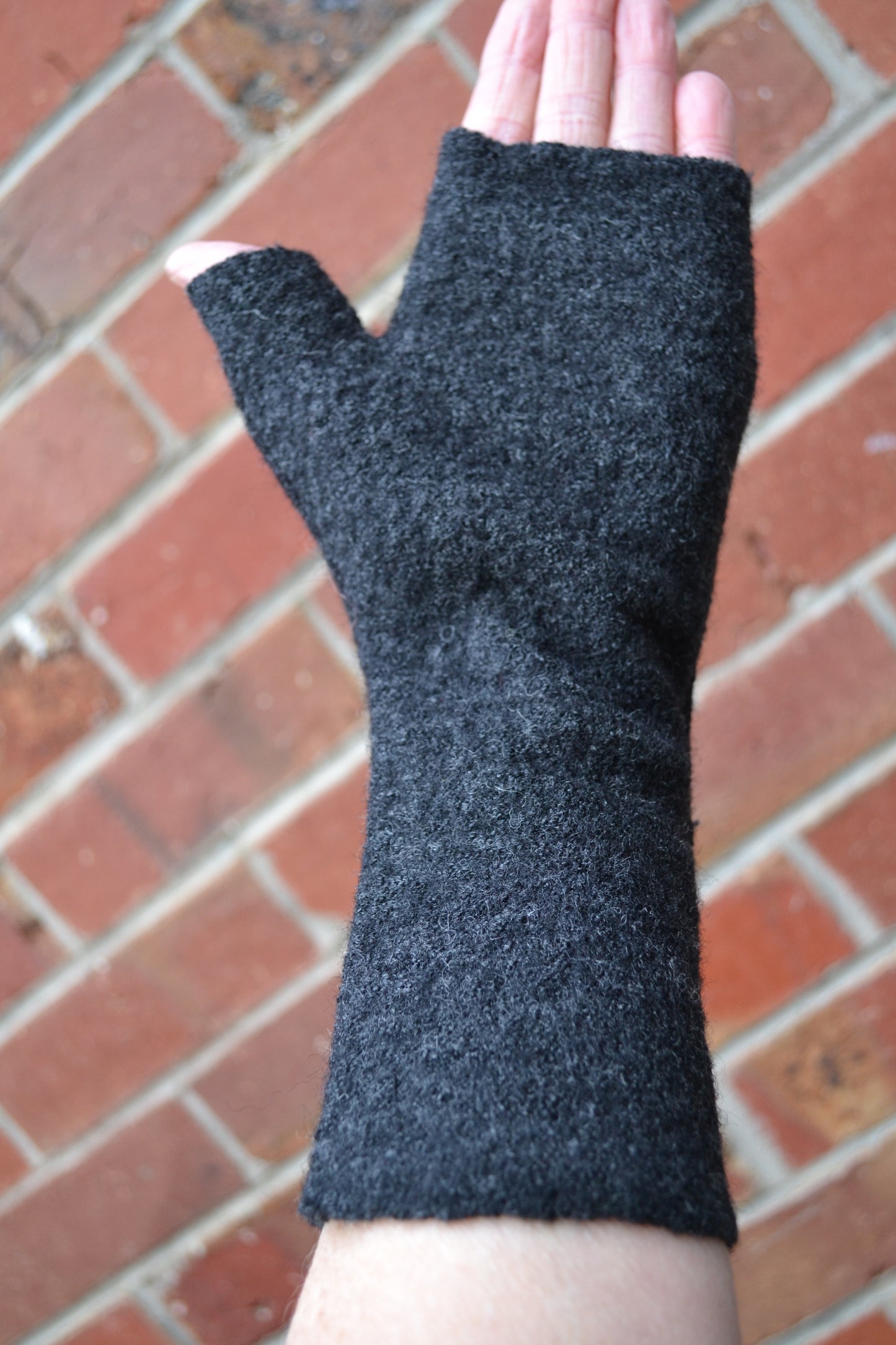 Black fingerless glove on a person's hand against a brick wall background