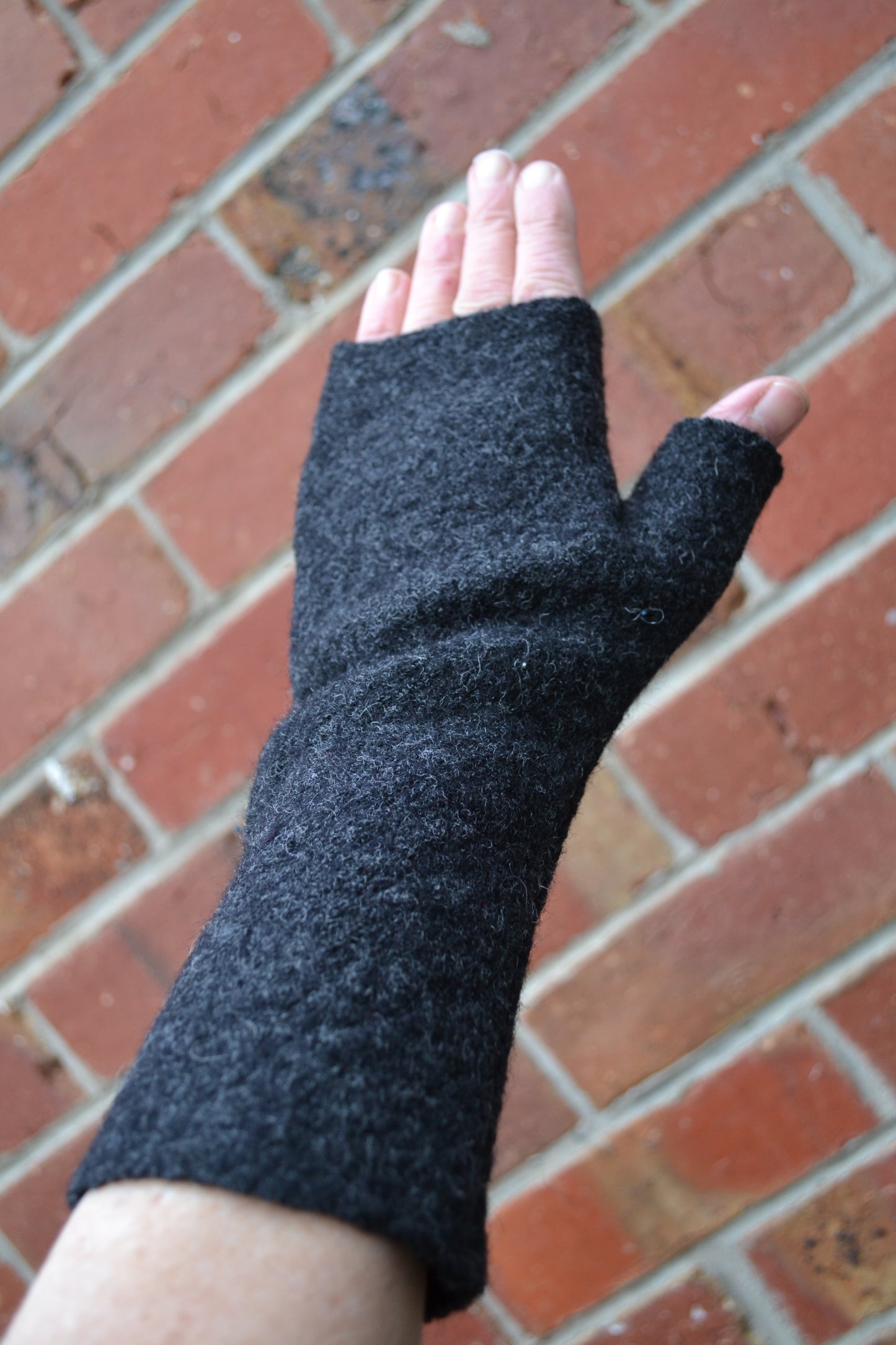 Black fingerless glove on a hand against a brick background